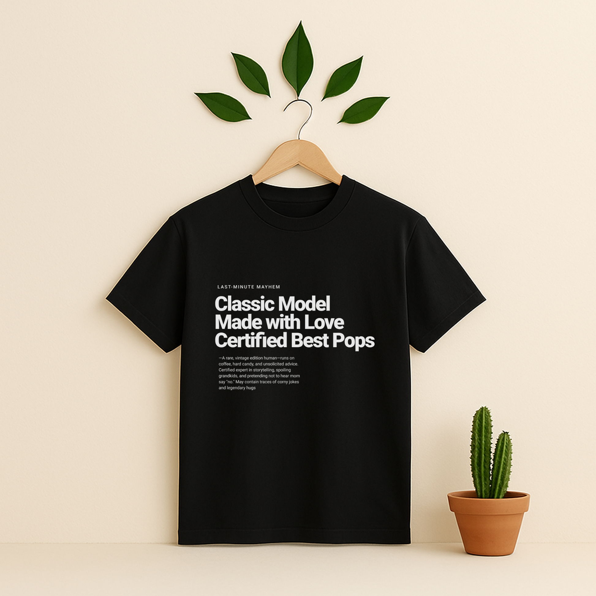 Black t-shirt with text on a hanger against a beige background with a potted Cactus plant.