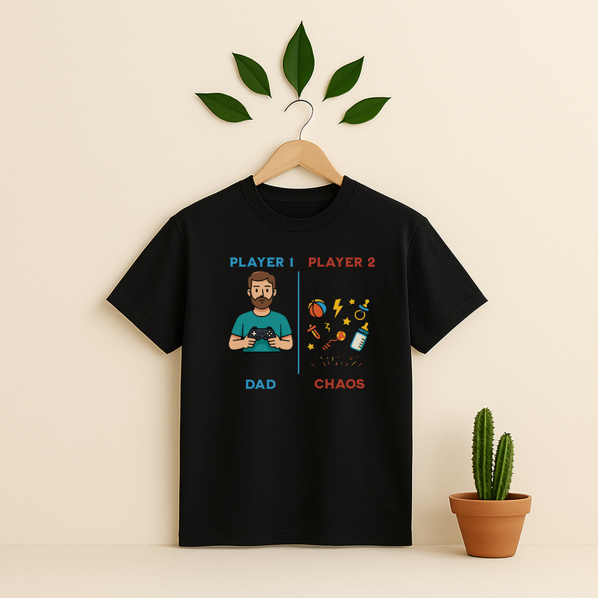 Black t-shirt with 'Player 1 & Player 2 Dad' graphic on a wooden hanger against a beige background with a cactus plant.