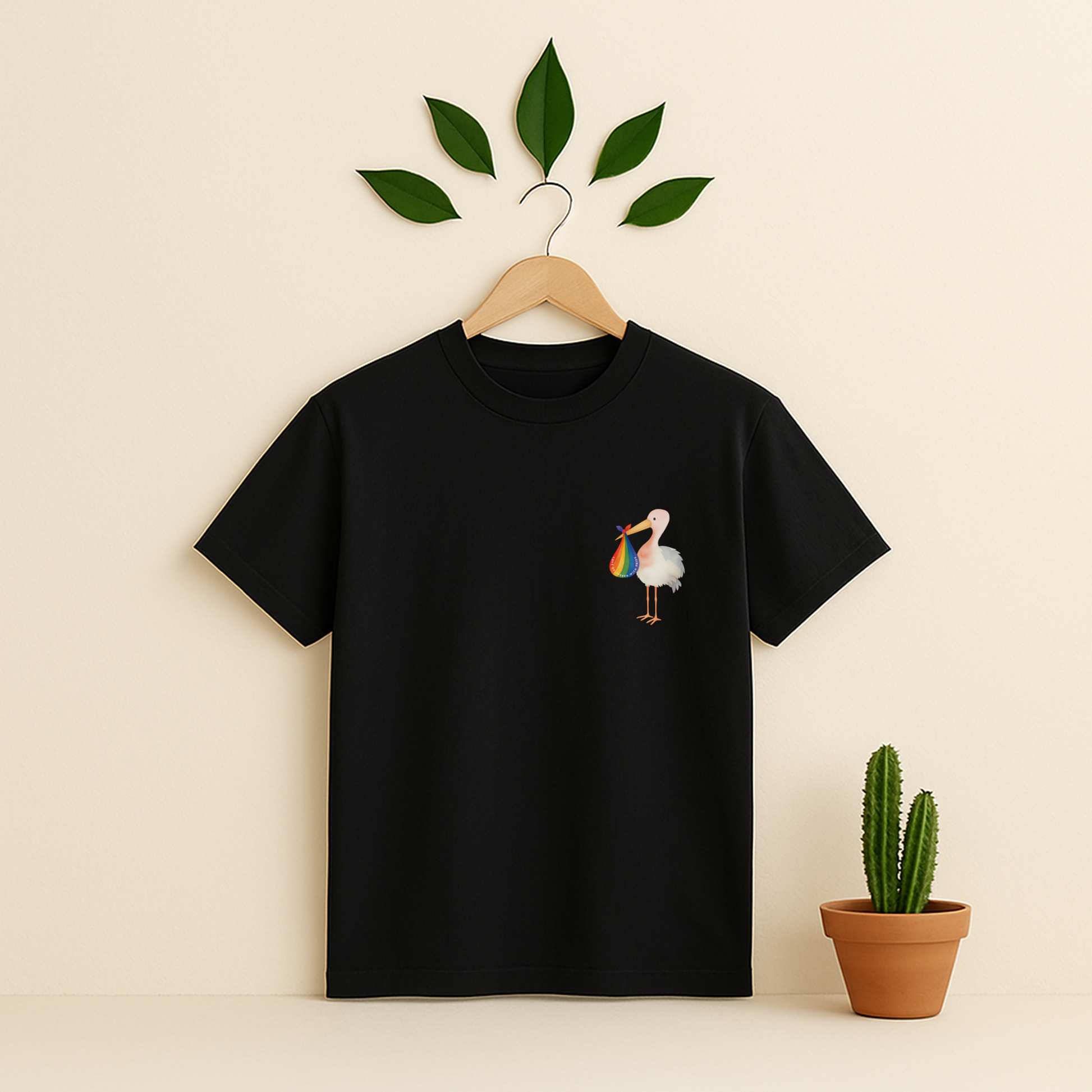 Black t-shirt with a colorful bird design on a wooden hanger against a beige background with a cactus plant.