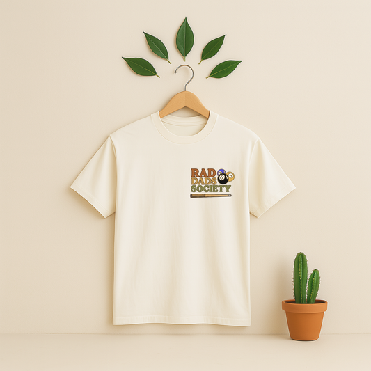 Ivory t-shirt with 'Rad Dads Society' graphic on a wooden hanger against a beige background with a cactus plant.