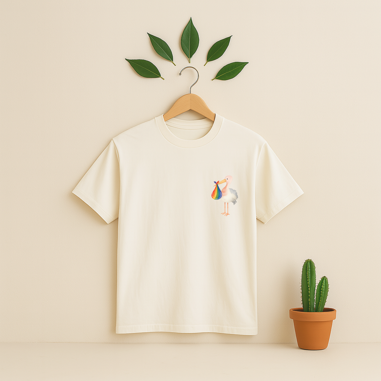 Ivory t-shirt with a colorful bird design on a wooden hanger against a beige background with a cactus plant.