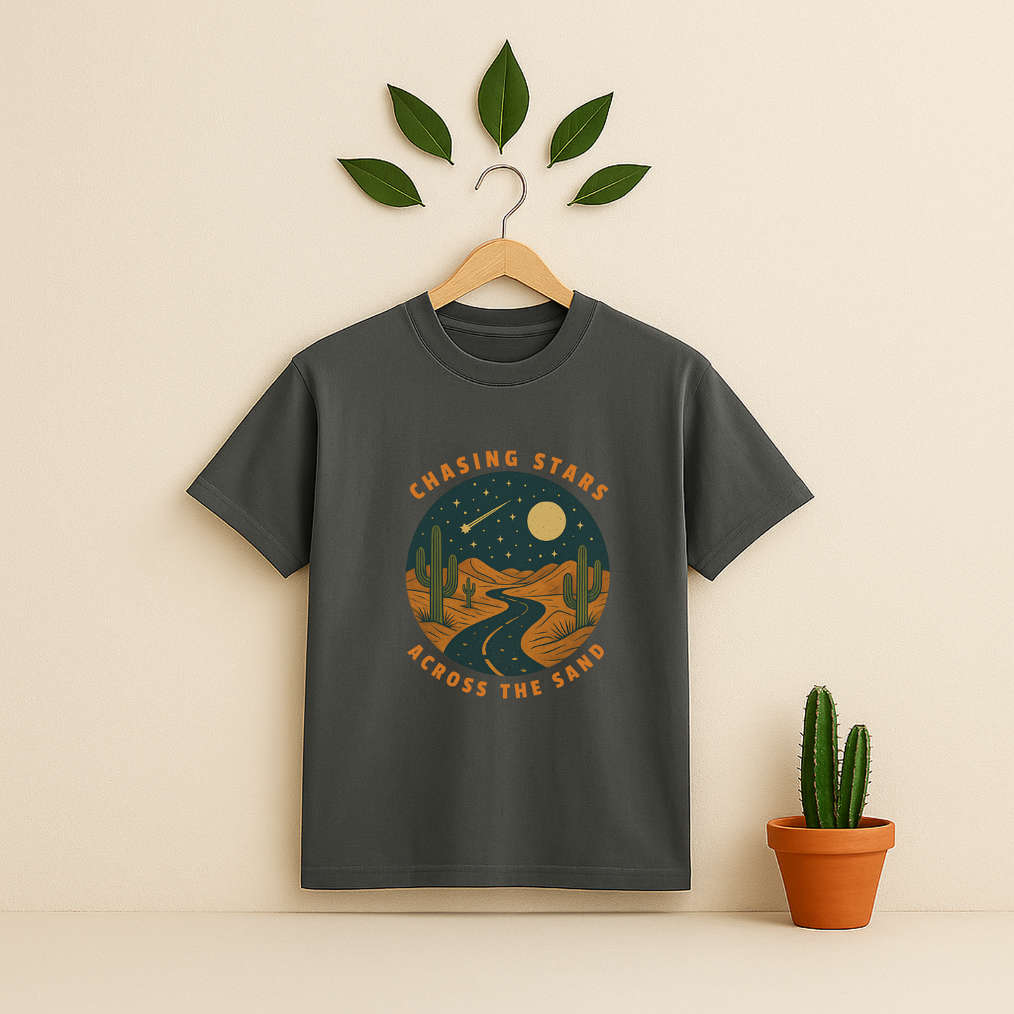 Pepper t-shirt with 'Chasing Stars Across the Sand' graphic on a wooden hanger against a beige background with a cactus plant.