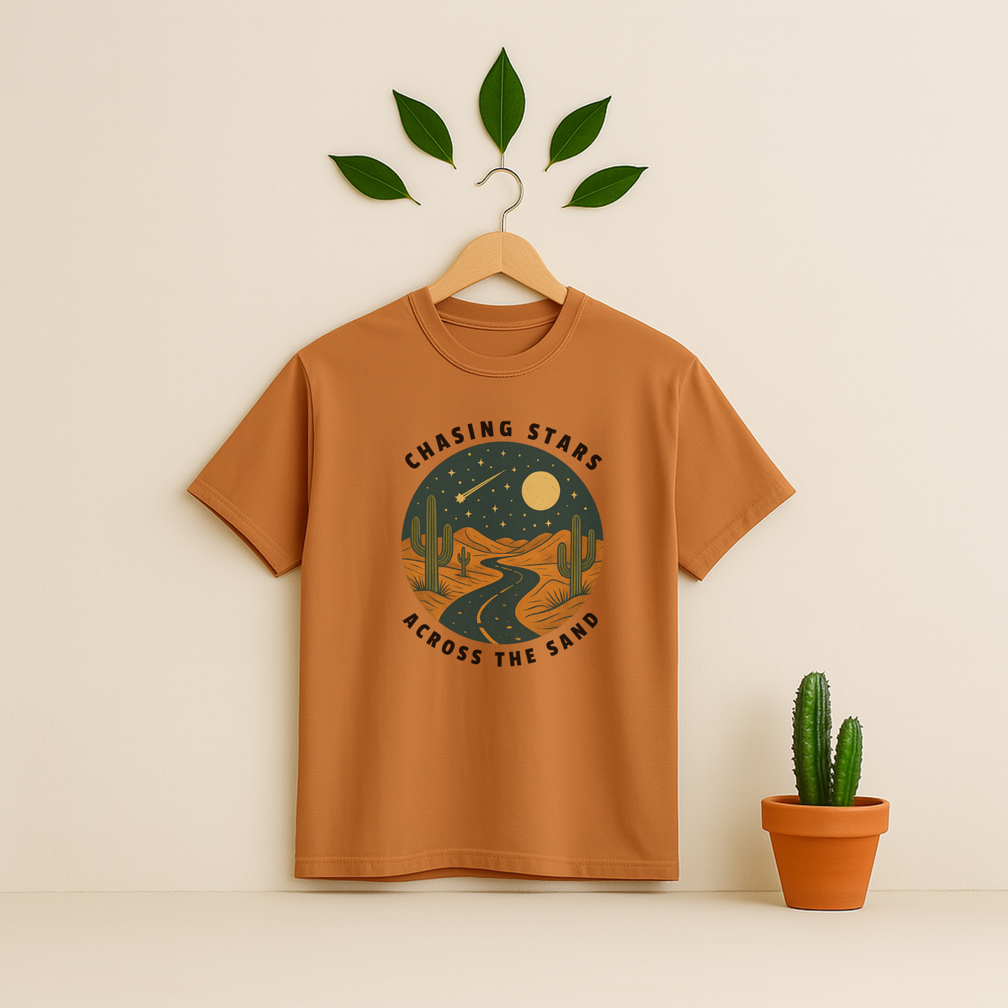 Yam t-shirt with 'Chasing Stars Across the Sand' graphic on a wooden hanger against a beige background with a cactus plant.