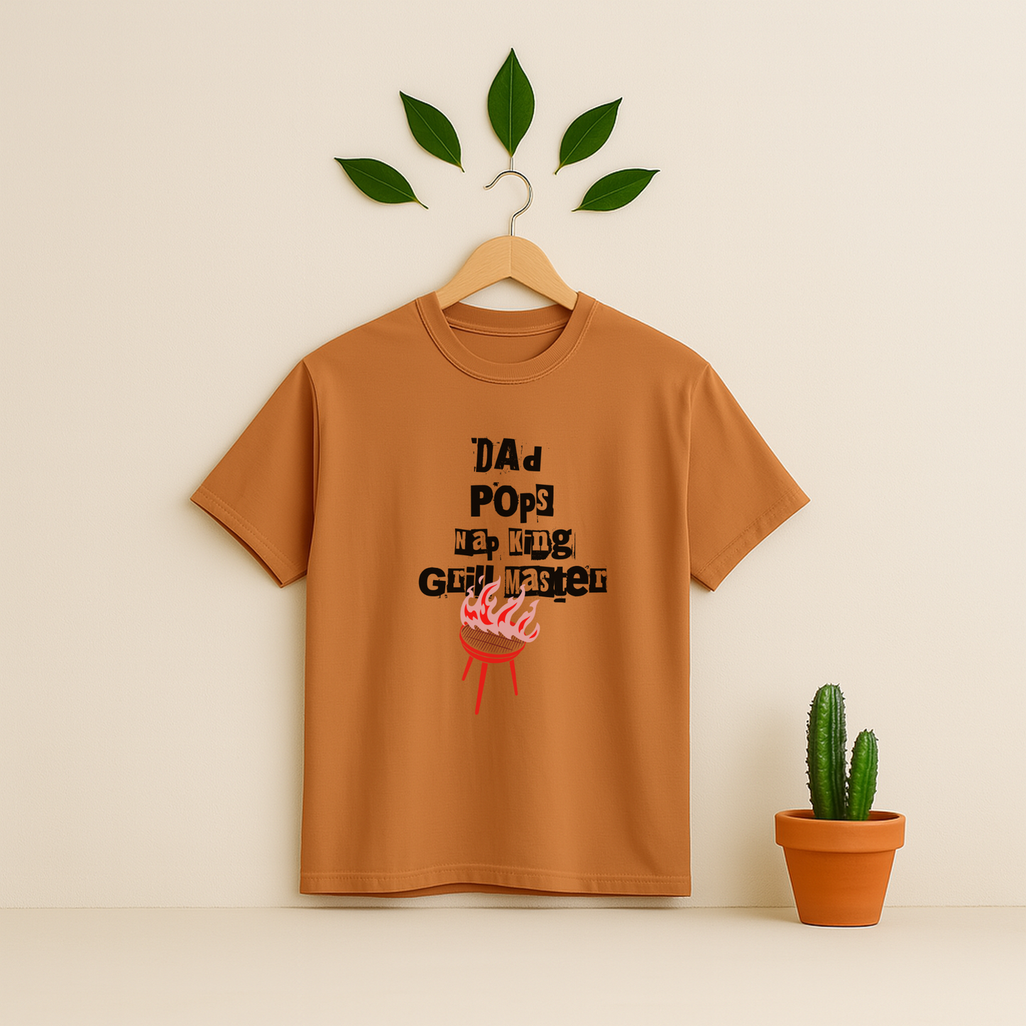 Yam t-shirt with 'Dad Pops Grill Master' graphic on a wooden hanger against a beige background with a cactus plant.