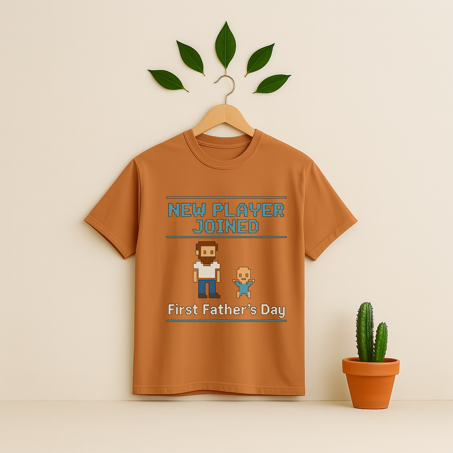Yam t-shirt with 'New Player Joined First Father's Day' graphic text and pixel art on a wooden hanger against a beige background with a cactus plant.
