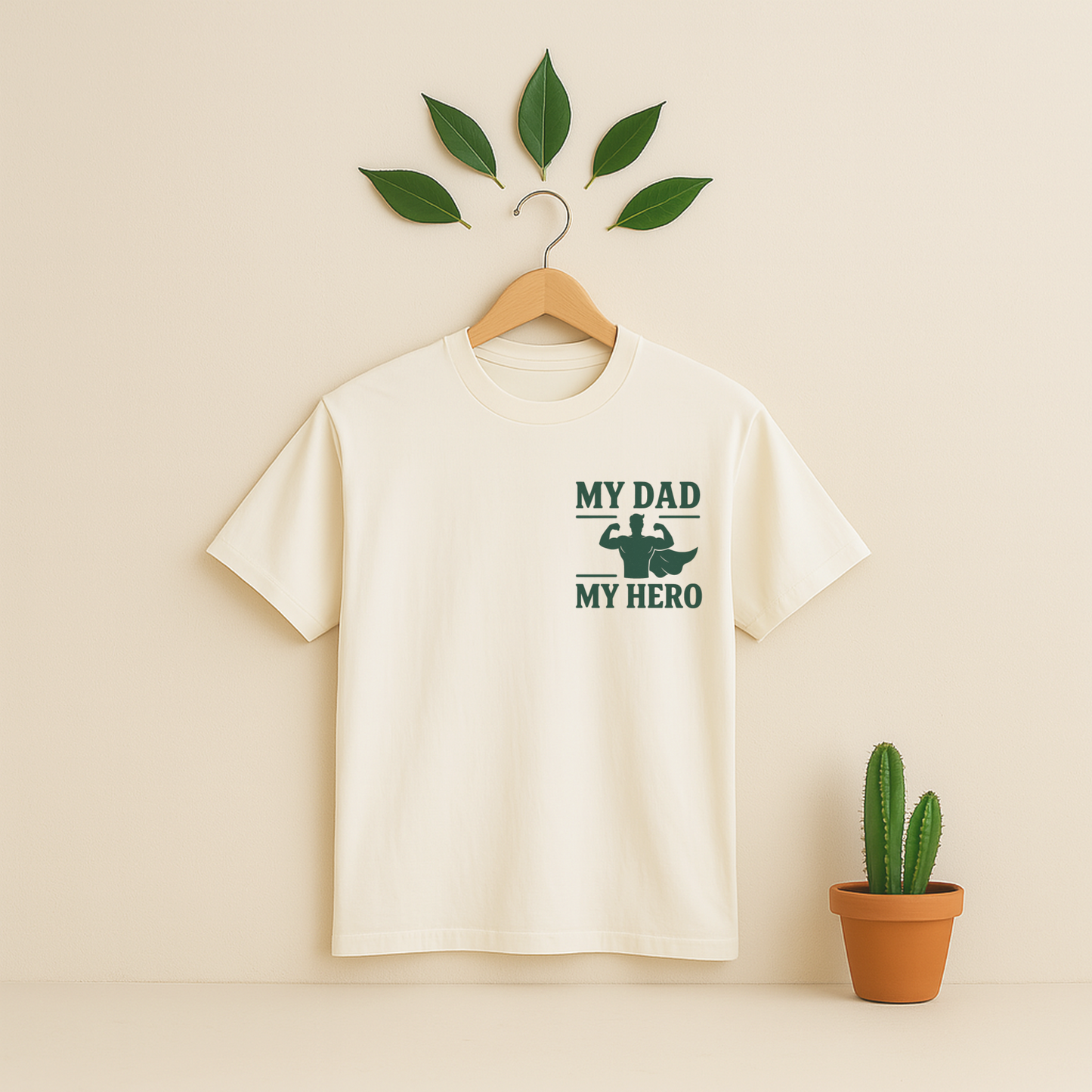 Ivory t-shirt with 'My Dad My Hero' graphic on a wooden hanger against a beige background with a cactus plant.