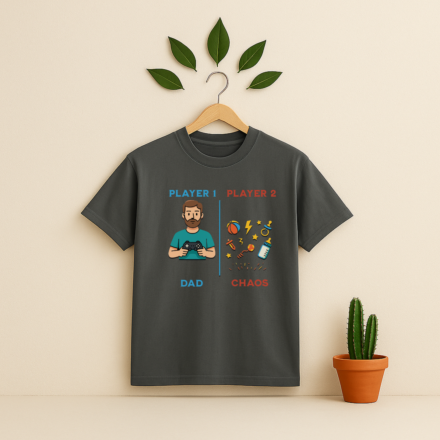 Pepper t-shirt with 'Player 1 & Player 2 Dad' graphic on a wooden hanger against a beige background with a cactus plant.